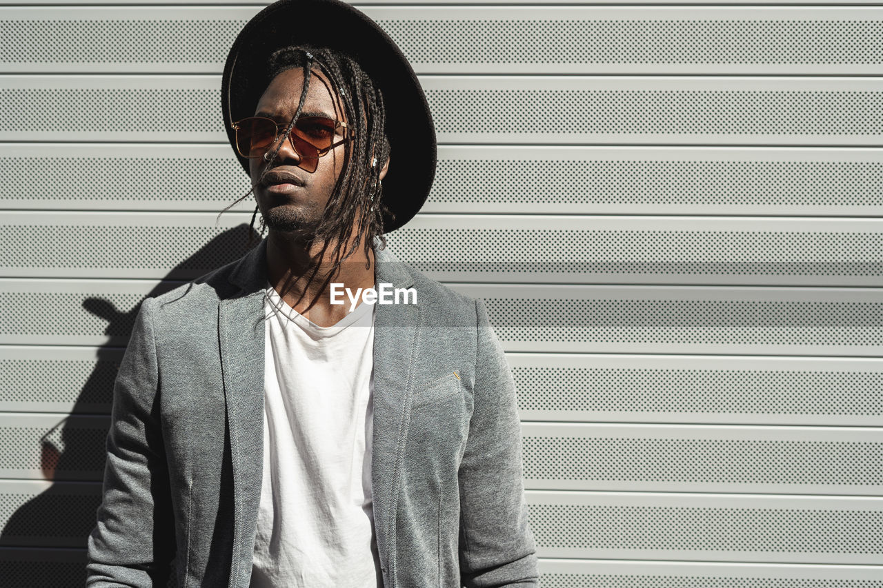 Young man wearing hat standing against shutter