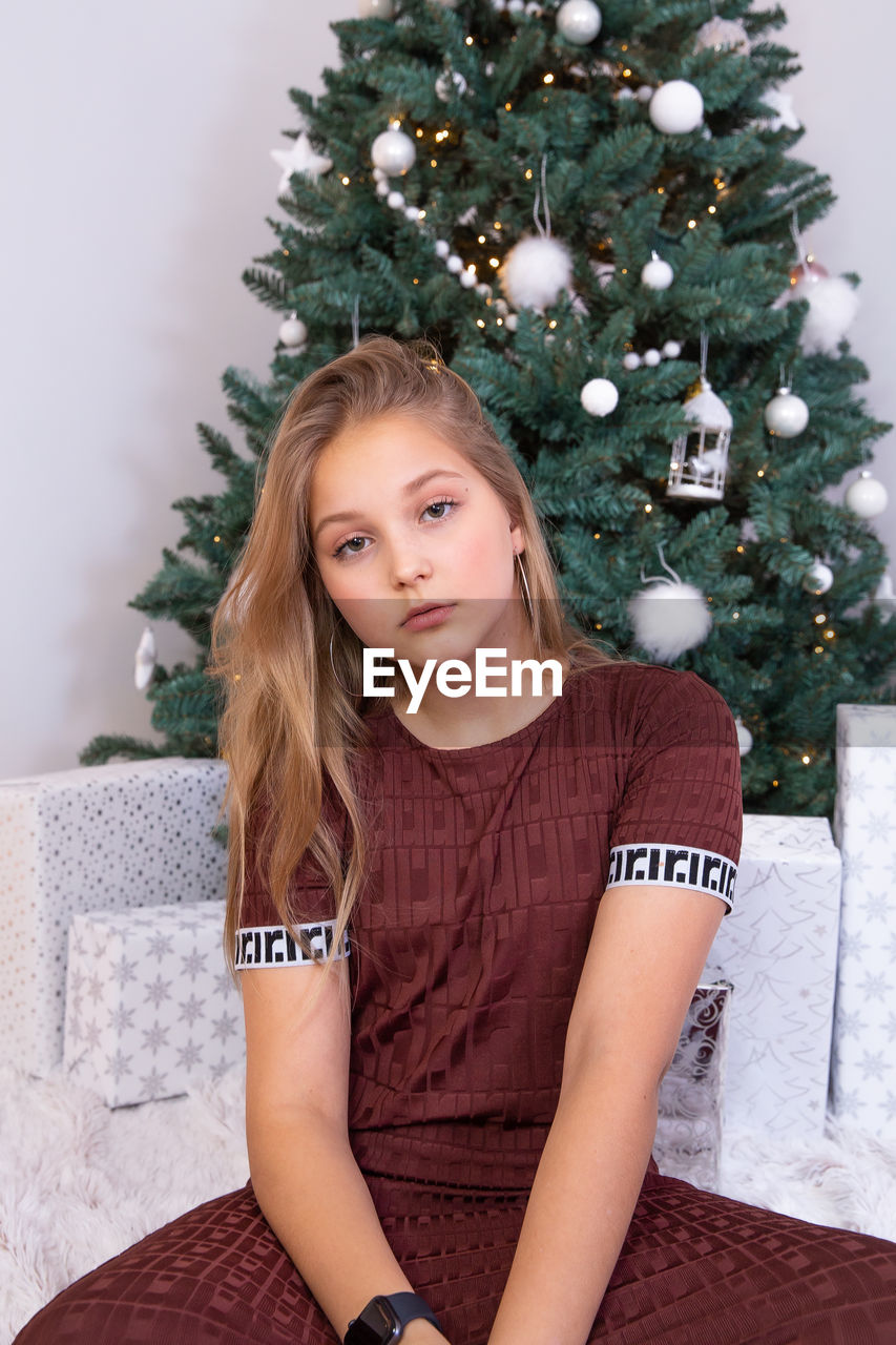 PORTRAIT OF A YOUNG WOMAN SITTING AGAINST TREE