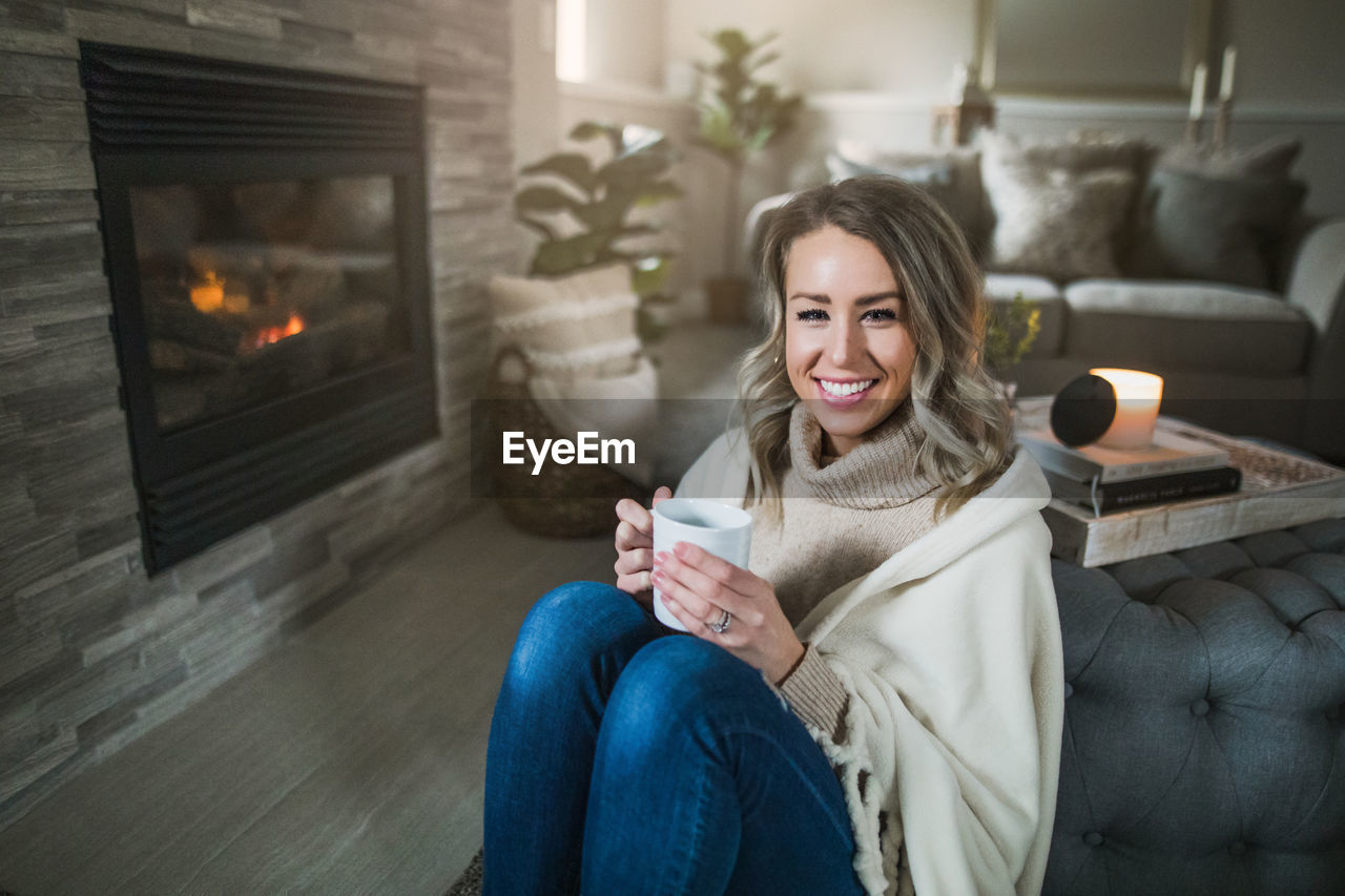 Portrait of smiling young woman holding coffee while sitting at home