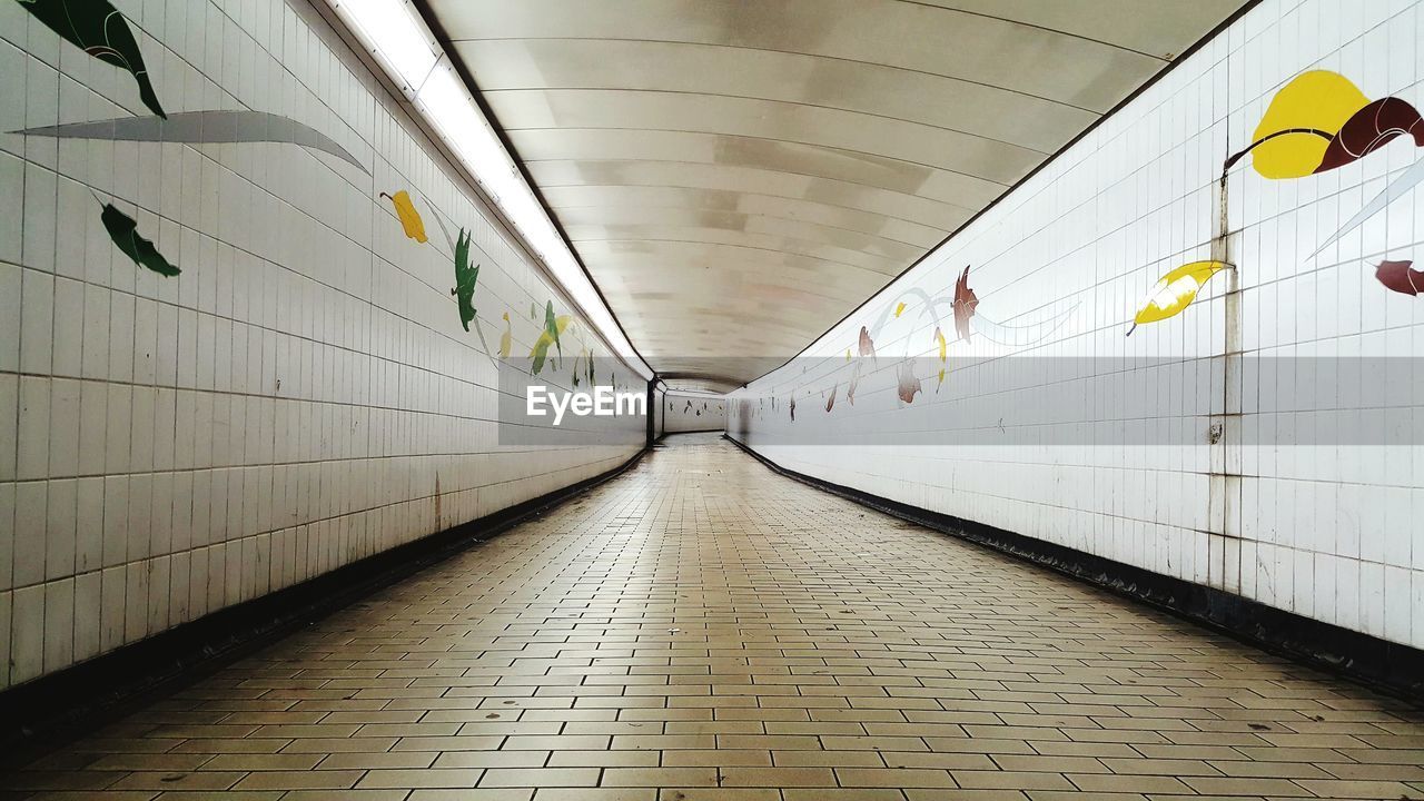 EMPTY CORRIDOR IN ILLUMINATED UNDERGROUND WALKWAY