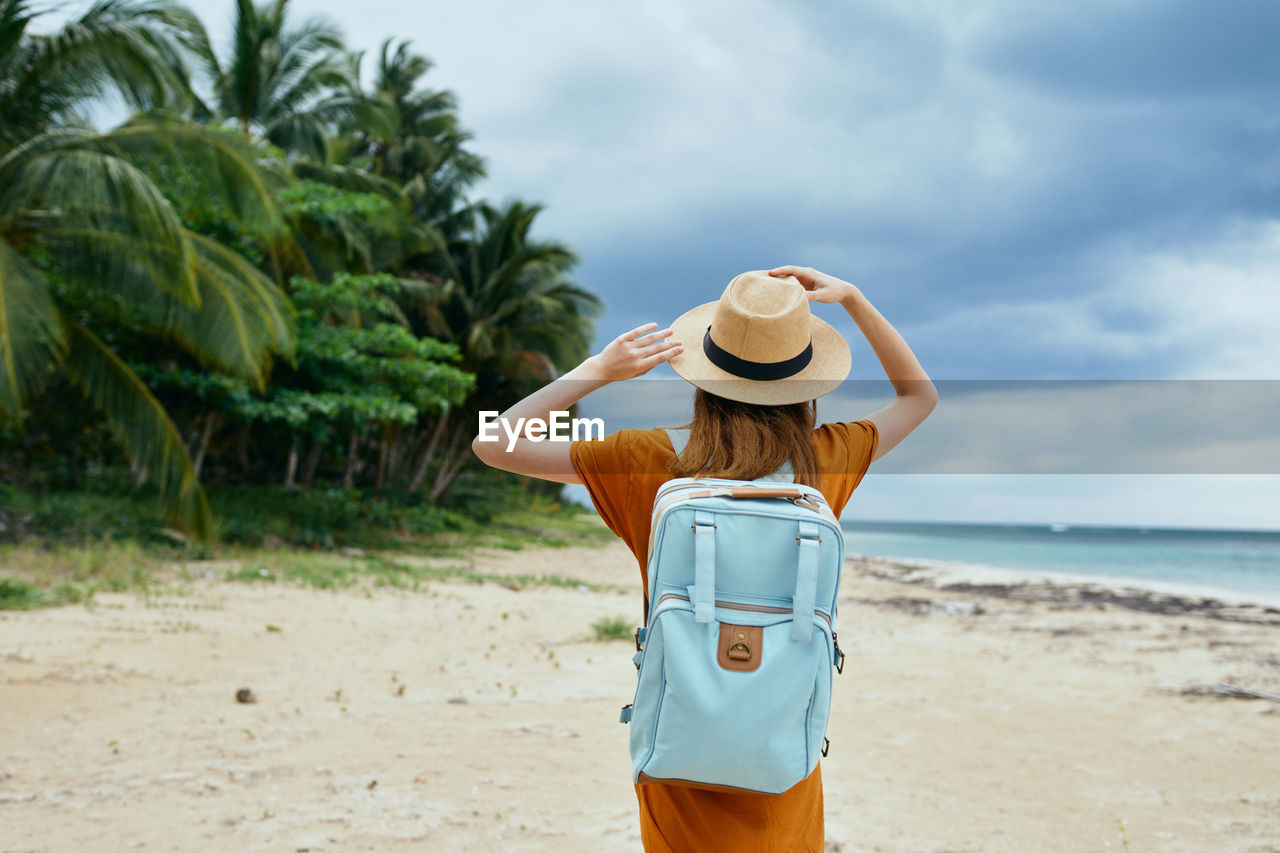 REAR VIEW OF WOMAN STANDING AT BEACH