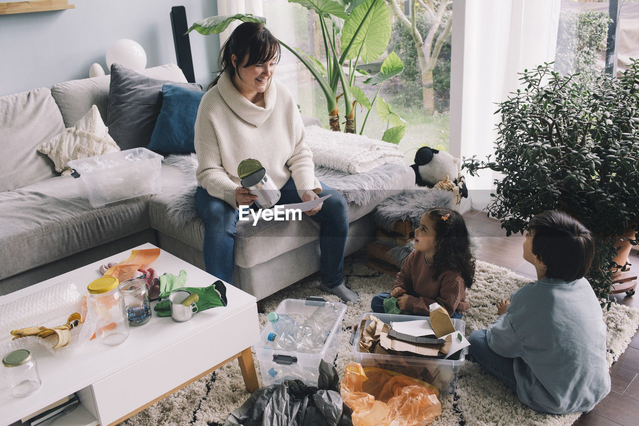 Smiling woman with son and daughter separating waste while sitting in living room