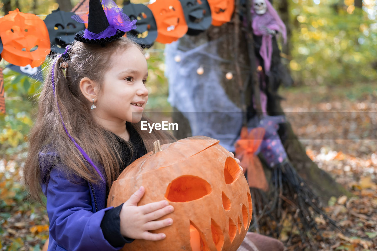 Halloween. cute little girl in witch costume with pumpkin having fun outdoor