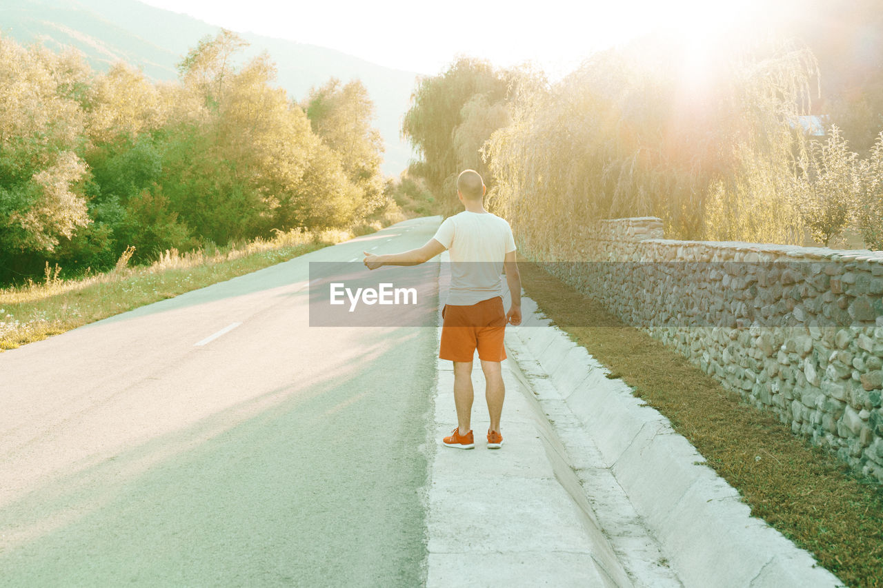 Rear view of man gesturing while standing on footpath by road