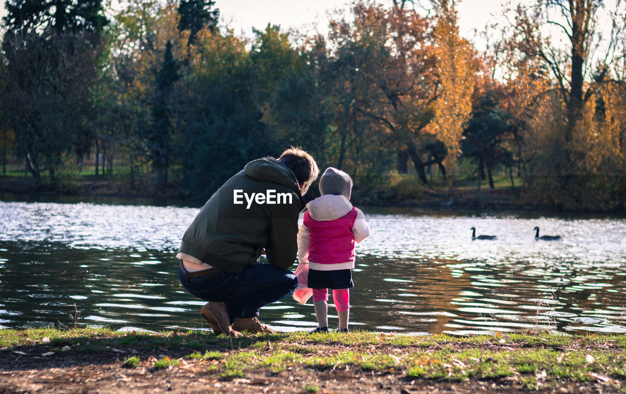 Rear view of man and child by lake by trees