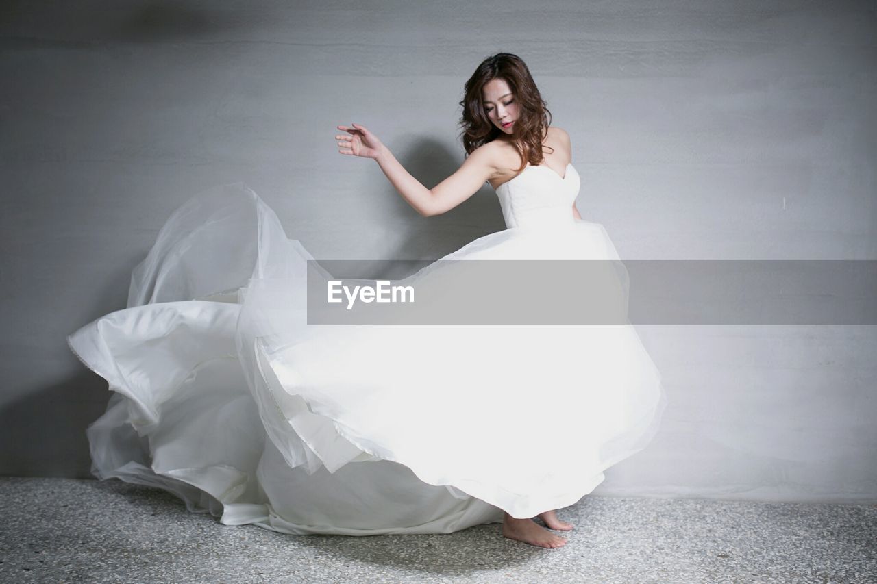 Beautiful woman wearing wedding dress while standing against wall