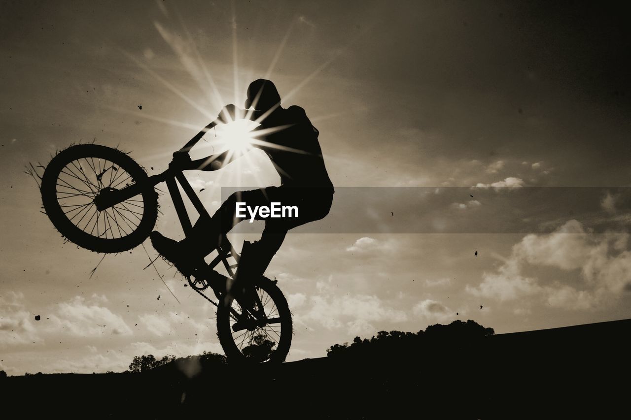 Low angle view of man performing stunt with bicycle against sky during sunset