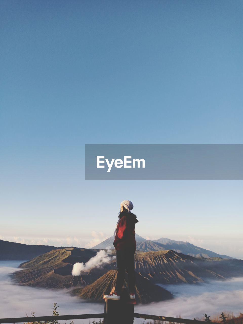 Young woman looking away while standing on railing against sky