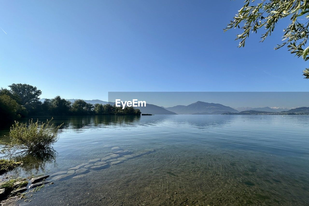 water, sky, scenics - nature, tree, nature, body of water, beauty in nature, reflection, lake, tranquility, environment, plant, landscape, mountain, morning, land, blue, tranquil scene, clear sky, shore, no people, travel destinations, travel, day, outdoors, coast, horizon, cloud, non-urban scene, beach, idyllic, sunlight, wilderness, tourism, forest, sunny, reservoir, pinaceae