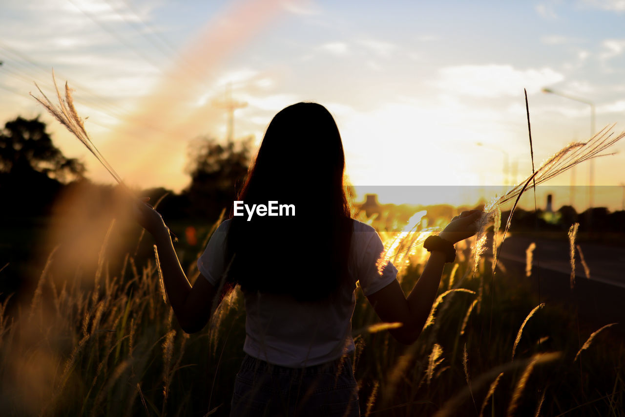 Rear view of woman standing on field against sky during sunset