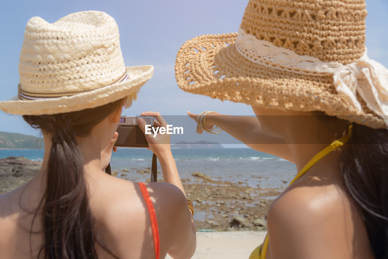 Rear view of women in hat photographing on beach