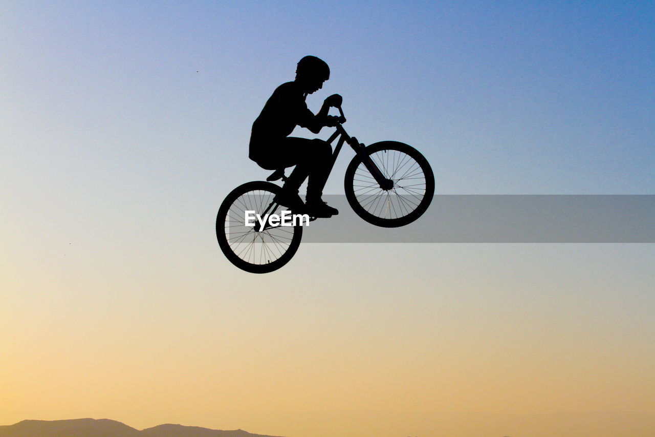 Man with bicycle jumping against clear sky