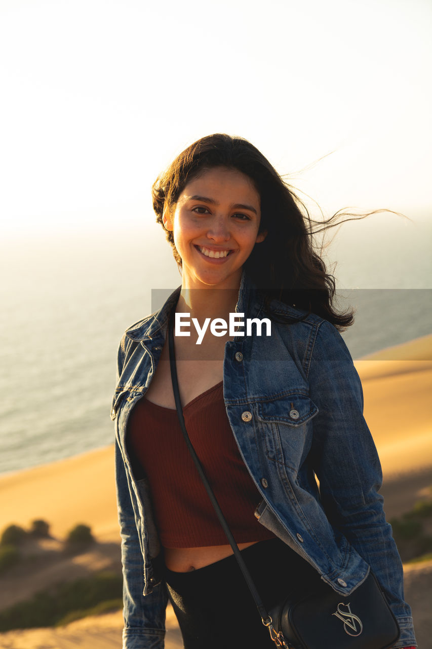 Portrait of smiling young woman standing against sky