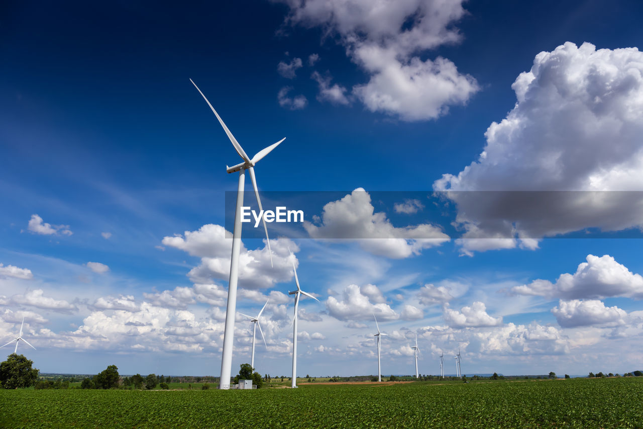 Low angle view of windmills on field against cloudy sky