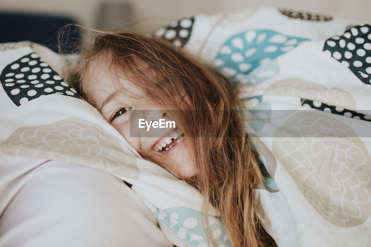 Smiling girl wrapped in blanket on bed at home