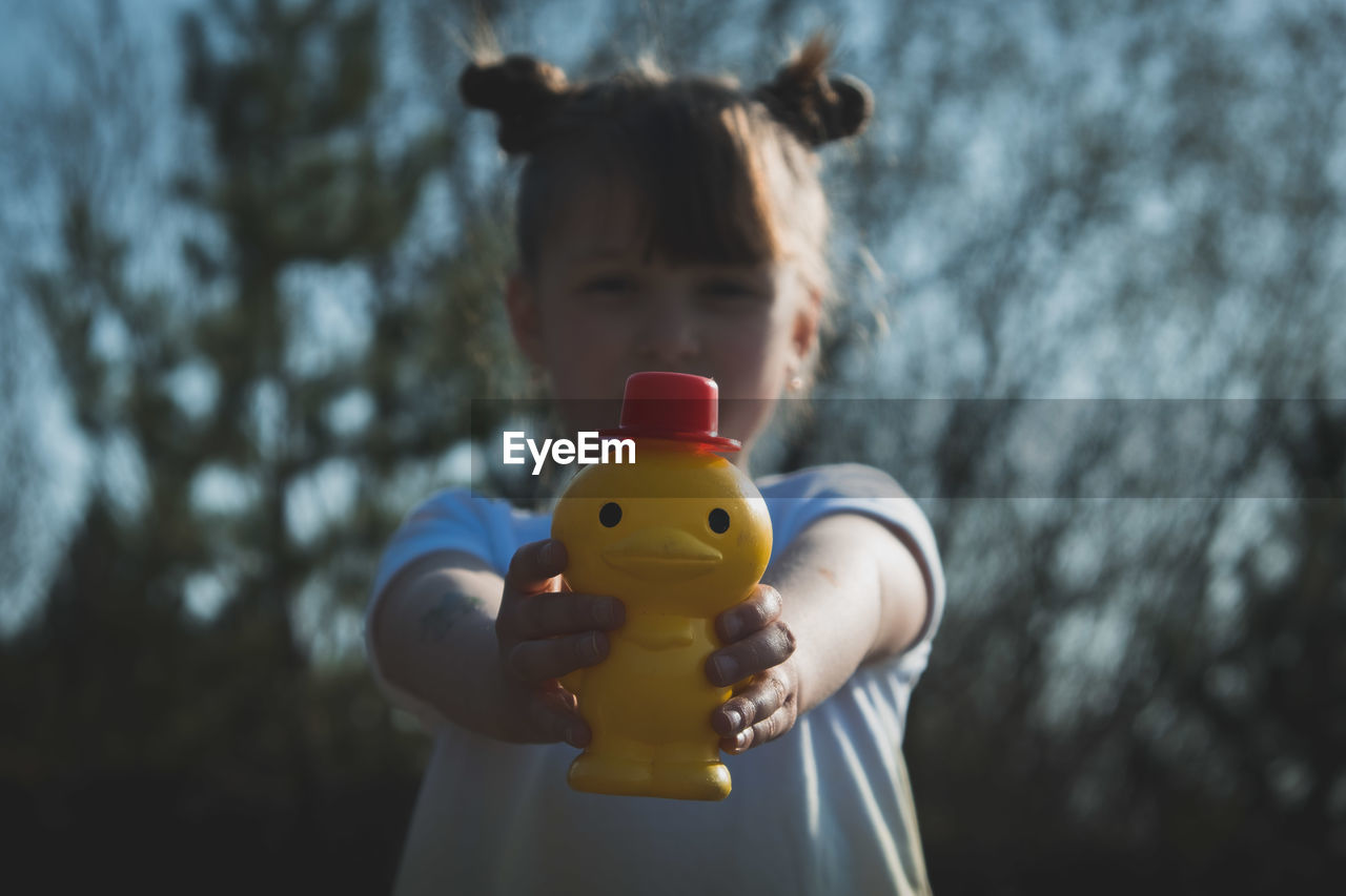 Portrait of girl holding toy against trees