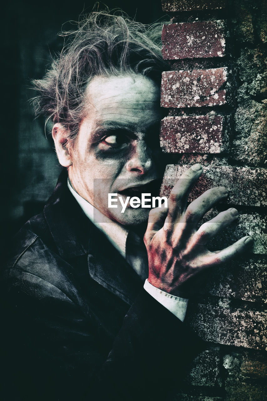 Spooky man with face paint leaning on brick wall