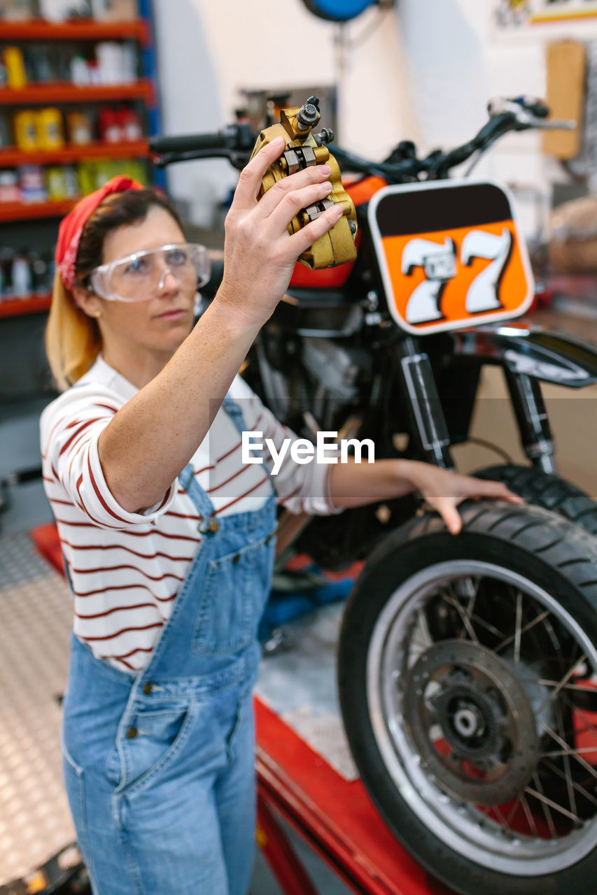 Mechanic woman checking motorbike caliper brake system on factory