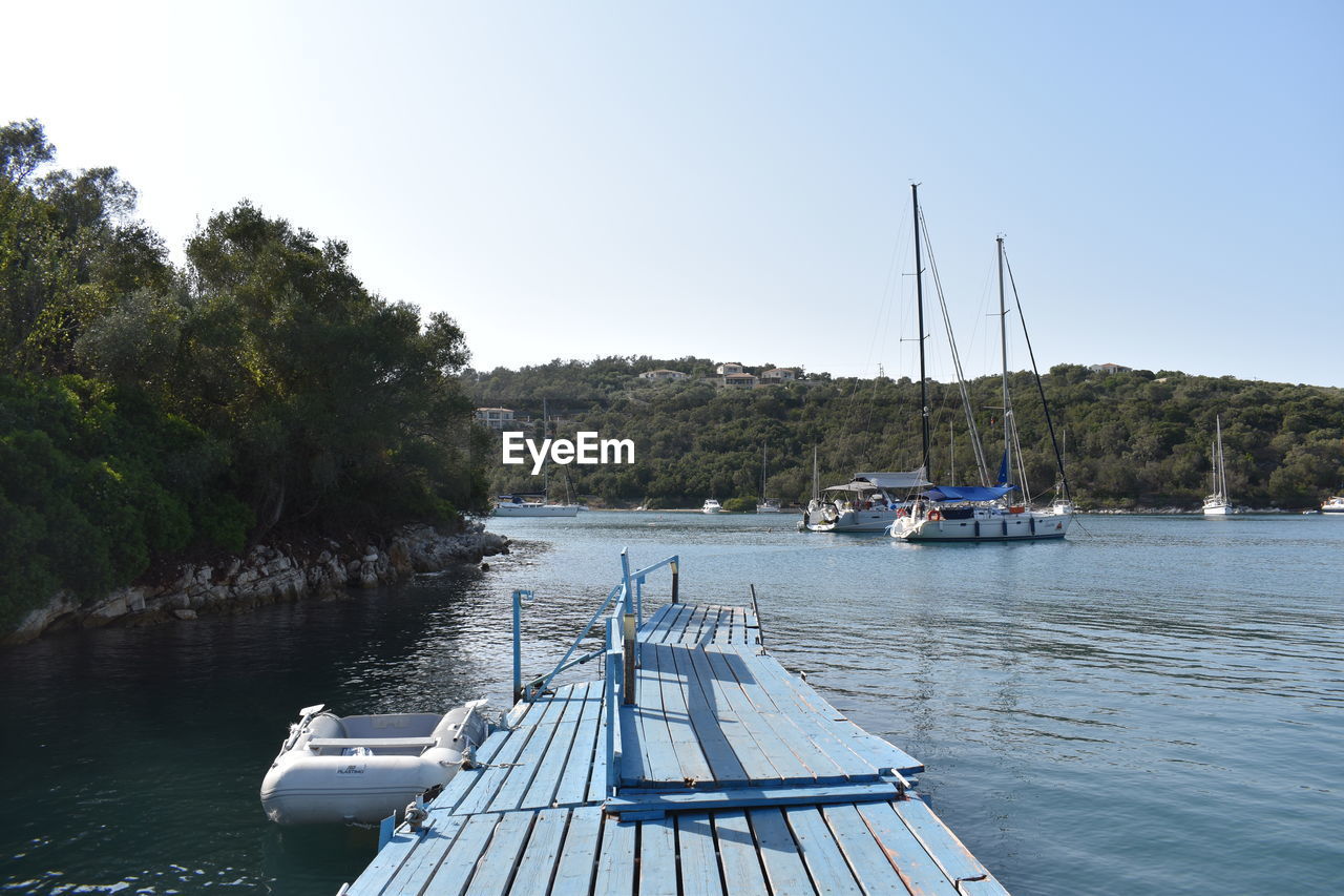 water, nautical vessel, transportation, mode of transportation, dock, sky, nature, boat, tree, vehicle, sea, tranquility, marina, travel, bay, sailboat, beauty in nature, scenics - nature, plant, ship, clear sky, no people, tranquil scene, day, travel destinations, holiday, pier, vacation, trip, land, moored, outdoors, boating, watercraft, idyllic, tourism, beach, environment, blue, non-urban scene, jetty, summer, landscape, sailing, channel, harbor, mast, yacht, sunny, sunlight, architecture, wood, pole