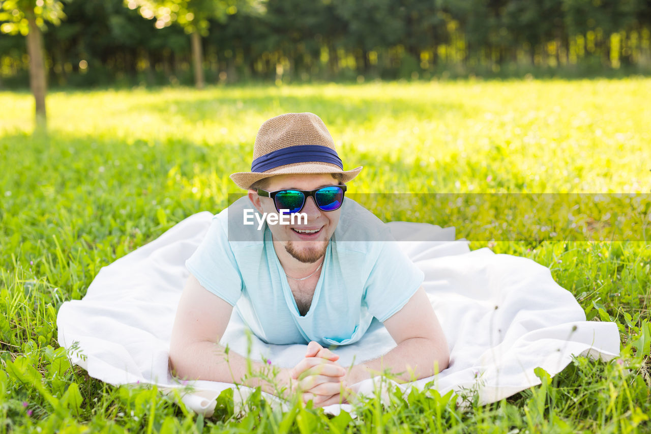 FULL LENGTH OF SMILING YOUNG WOMAN WEARING SUNGLASSES ON FIELD