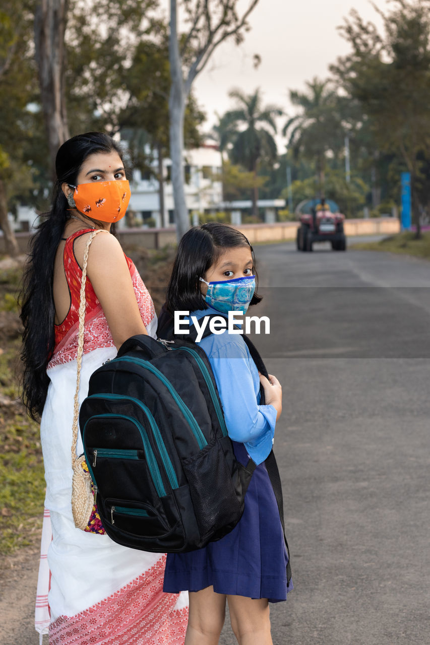 An indian school girl child going to school again after pandemic with her mother wearing nose mask 