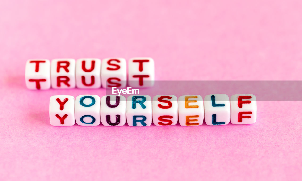 Quote trust yourself made out of colorful beads on pink background