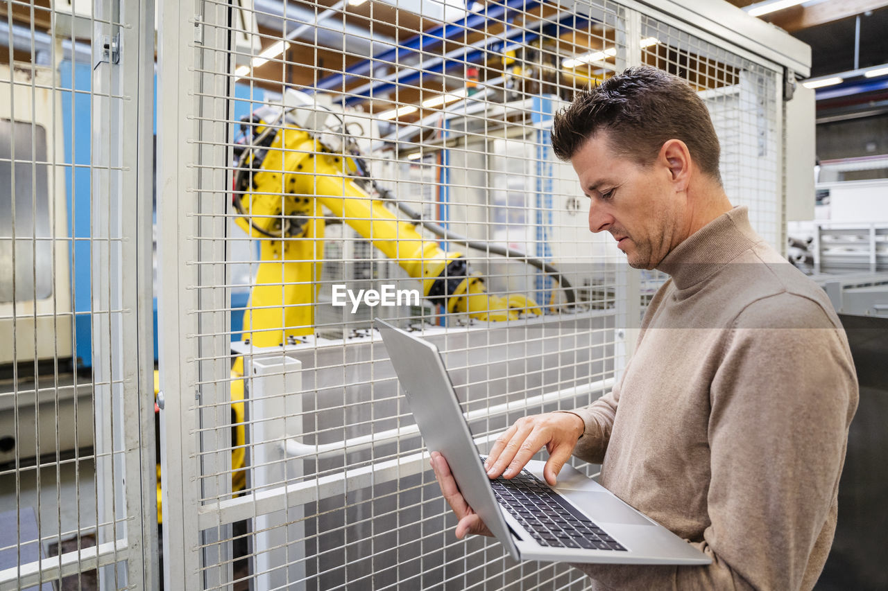 Mature businessman using laptop in front of robotic arm