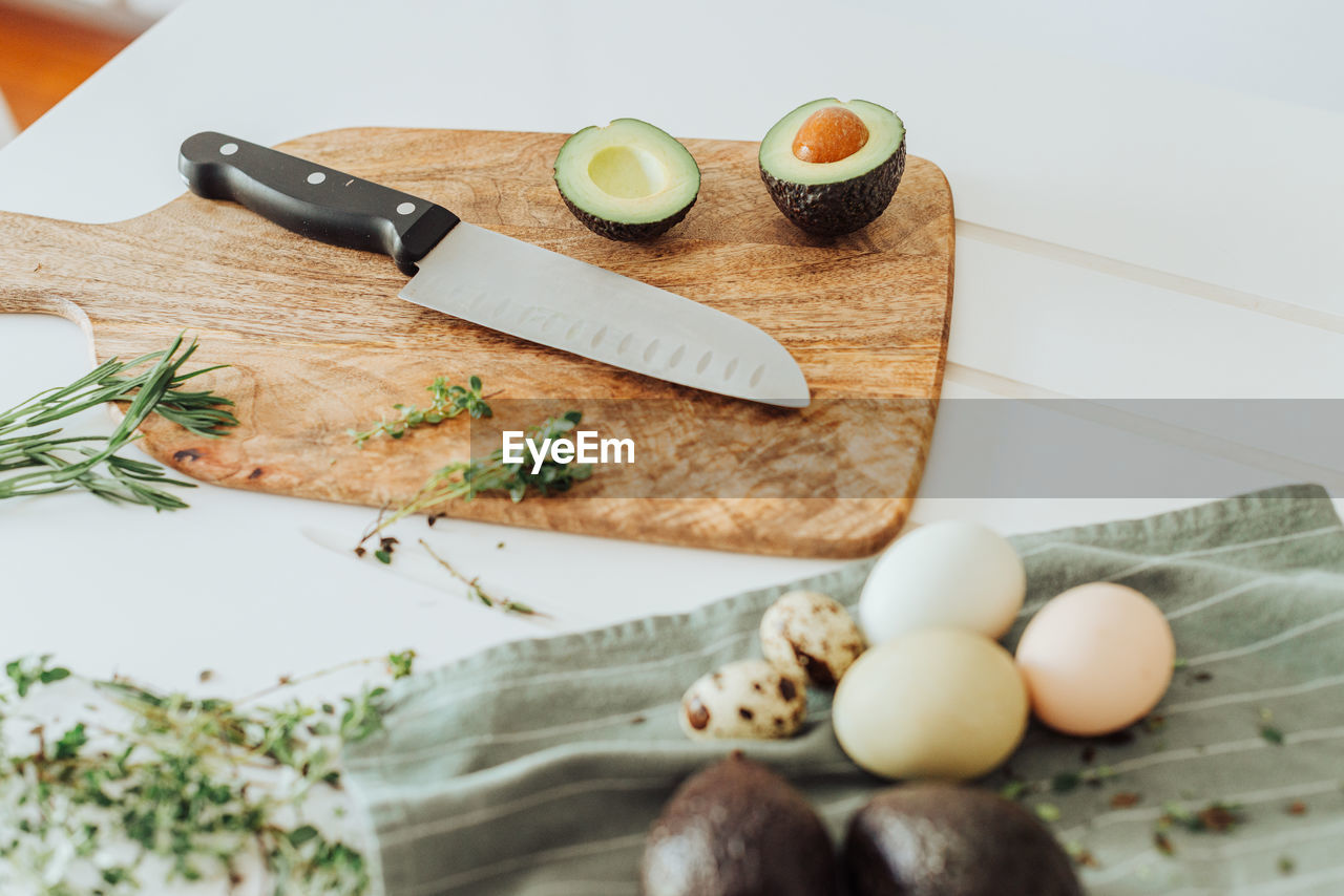 Cutting board with avocado, knife, thyme and rosemary and eggs