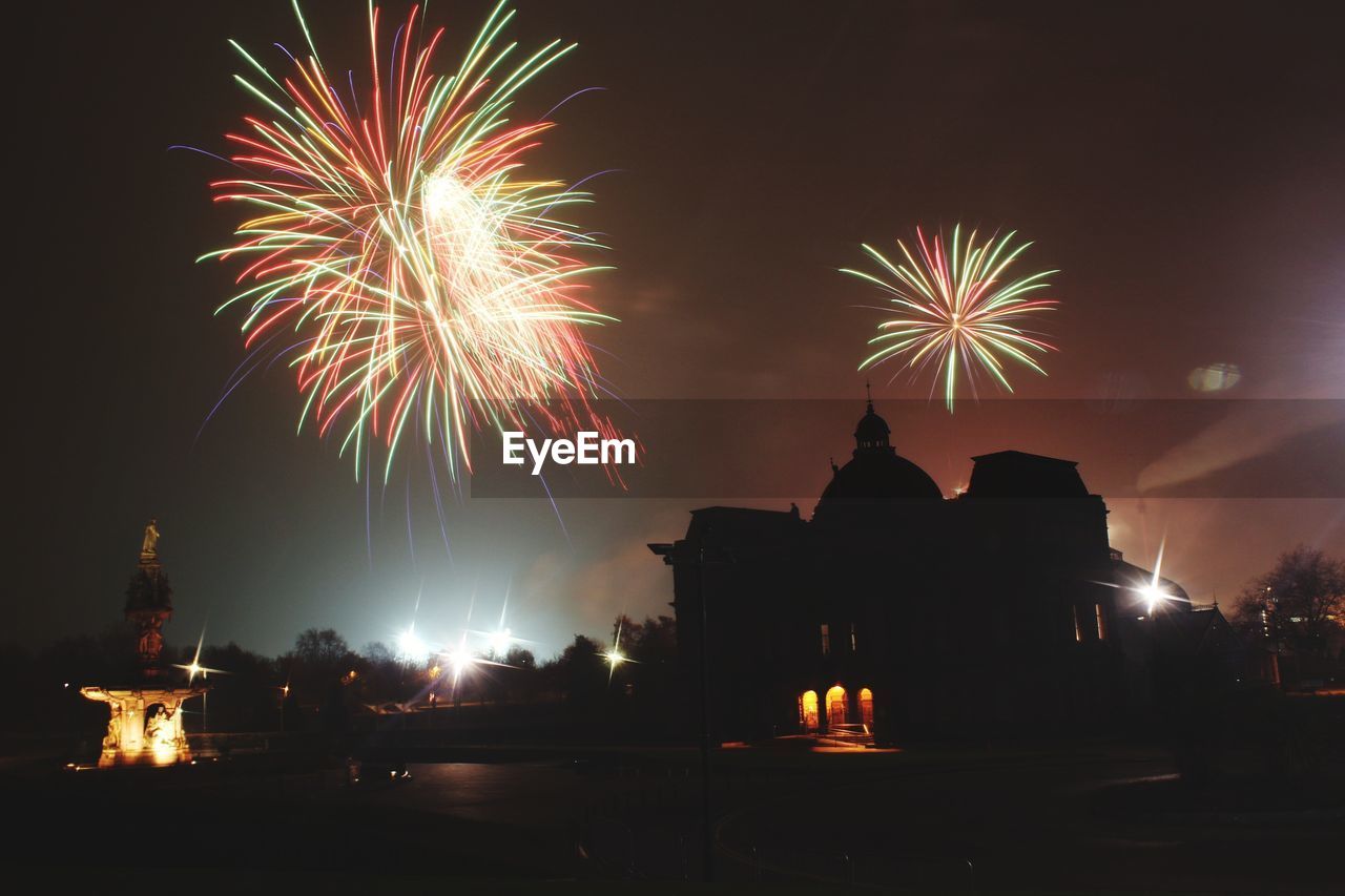 FIREWORK DISPLAY OVER ILLUMINATED BUILDING AGAINST SKY