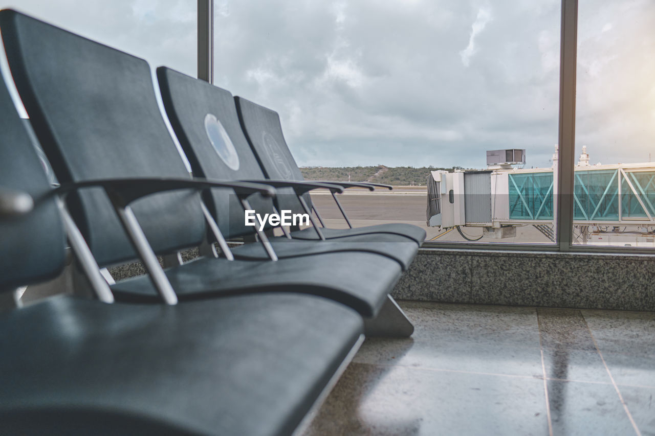 Empty chairs in the departure hall at airport, blurred plane on a background.