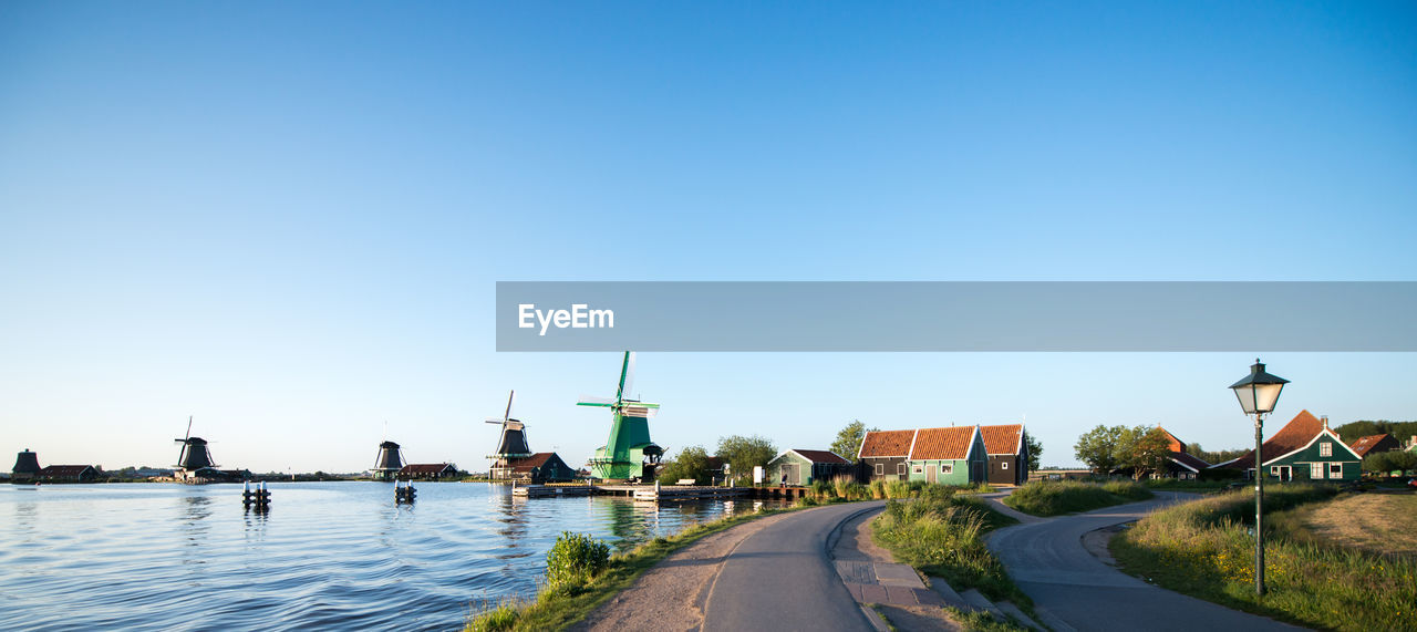 Empty roads and traditional windmills by canal against clear sky