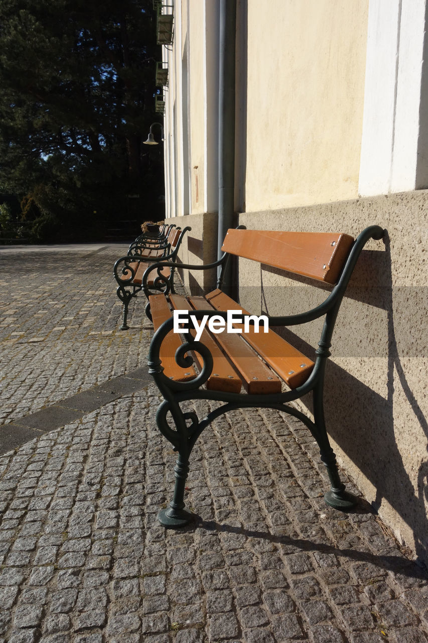 architecture, no people, wood, day, sunlight, footpath, iron, cobblestone, seat, furniture, built structure, building exterior, shadow, street, outdoors, floor, city, sidewalk, chair, absence, nature, flooring, empty, window, paving stone, building