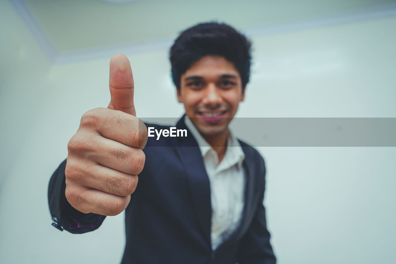 Portrait of smiling businessman showing thumbs up against wall