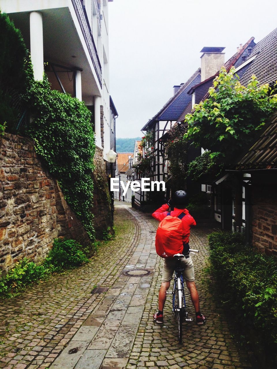 Rear view of man bicycling on narrow cobblestone lane against buildings