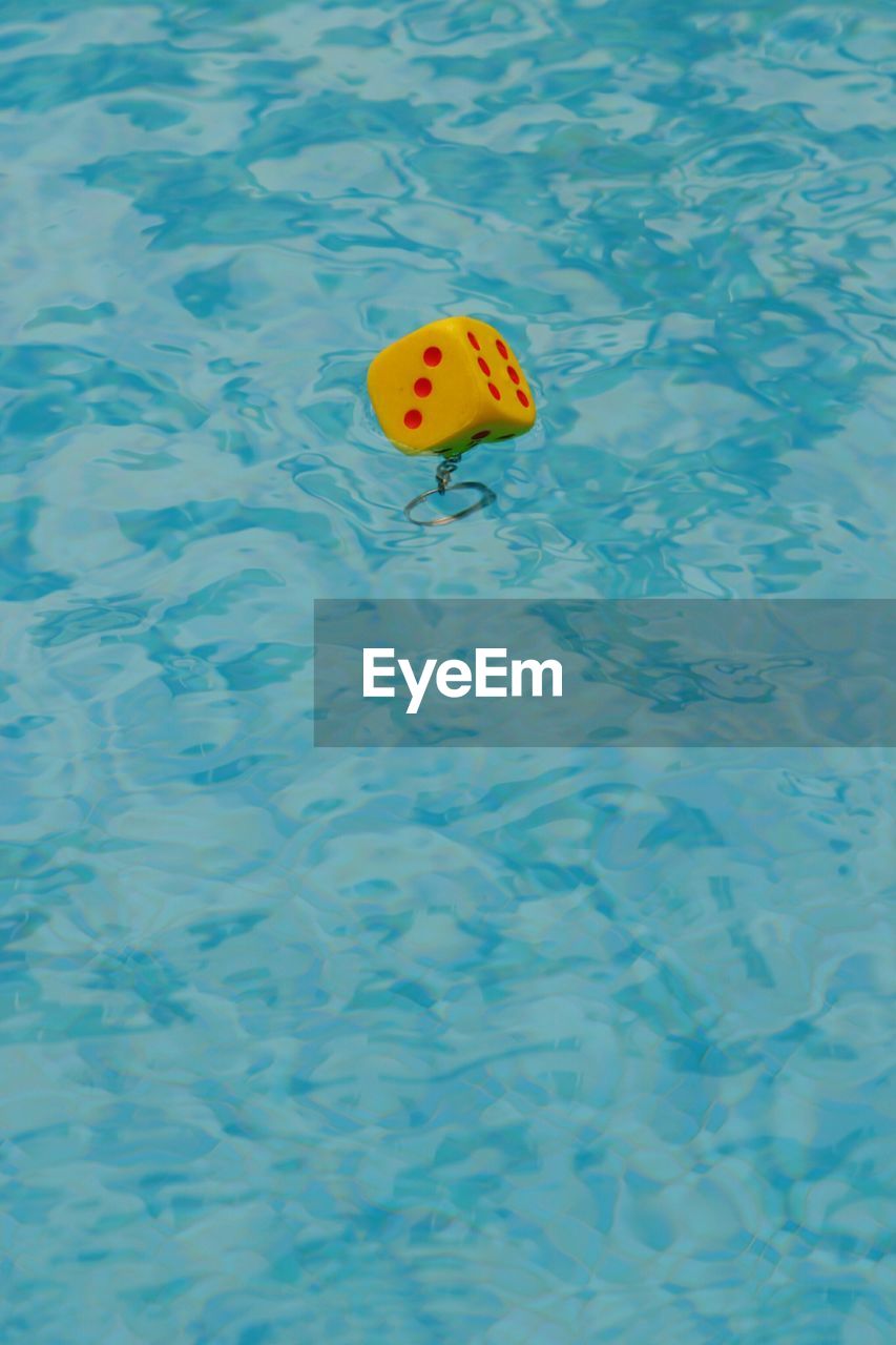 Yellow dice key ring floating on water in pool