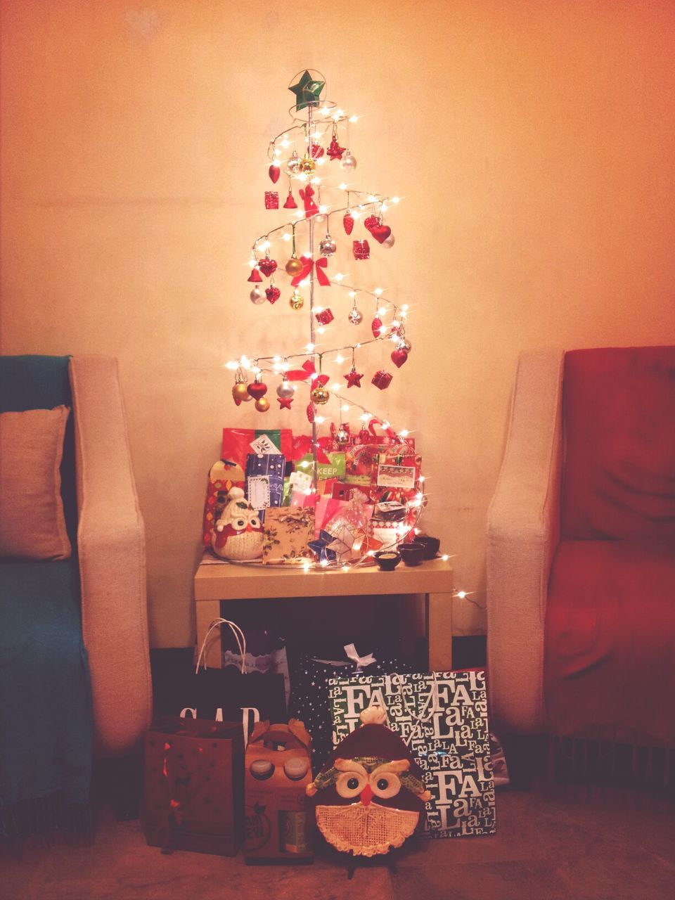 Illuminated christmas tree with presents in living room against wall