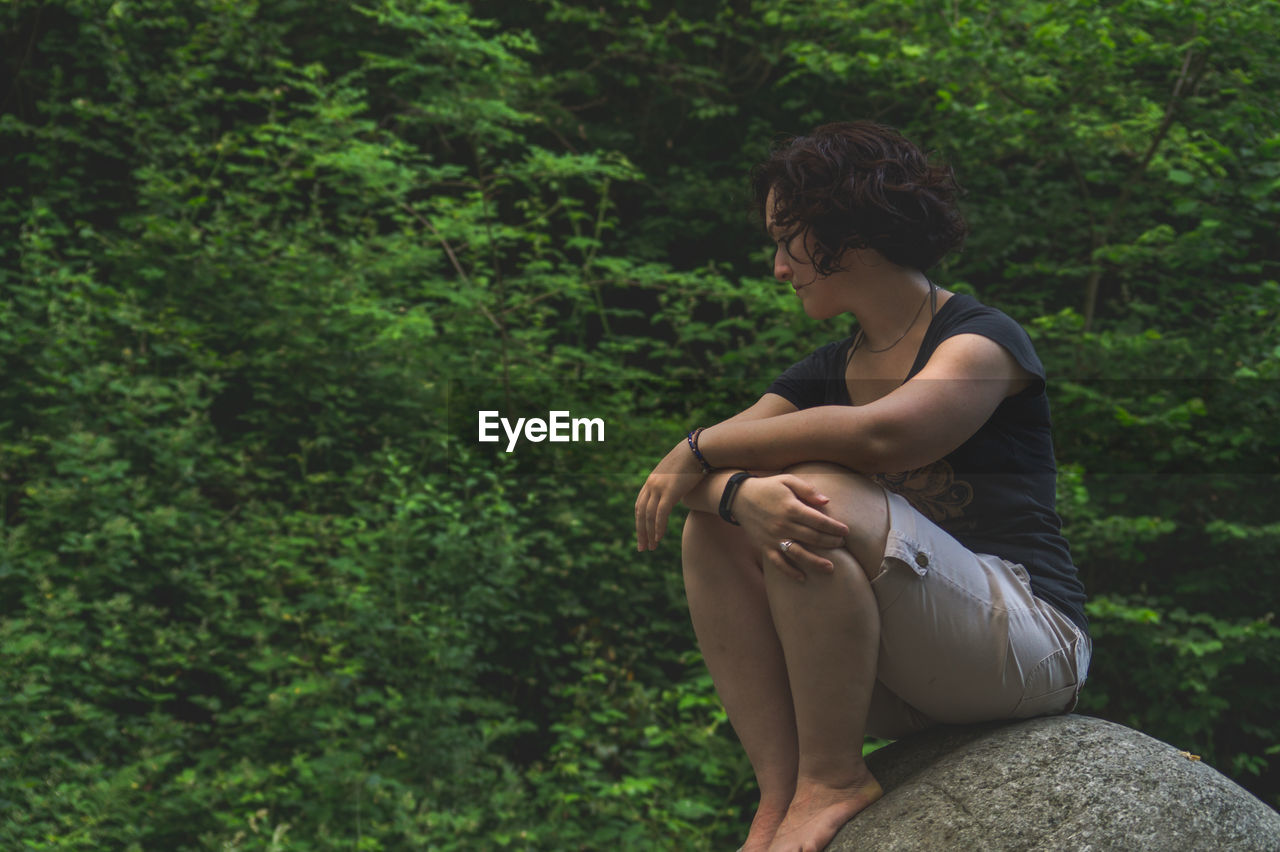 Side view of young woman sitting in forest