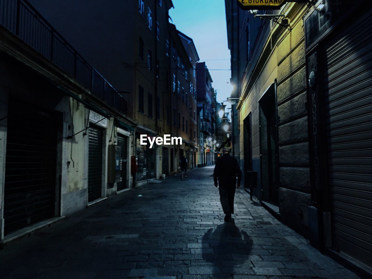 Rear view of man walking in lane amidst buildings in city