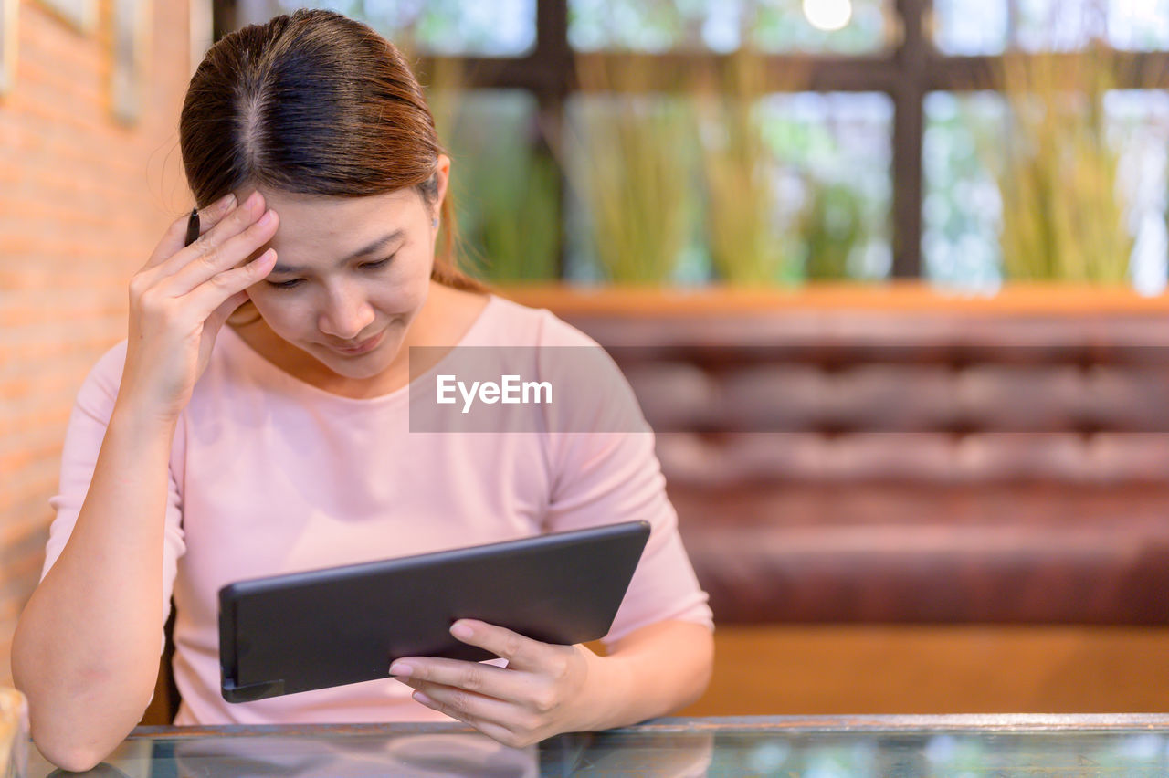 YOUNG WOMAN USING MOBILE PHONE WHILE SITTING ON SMART