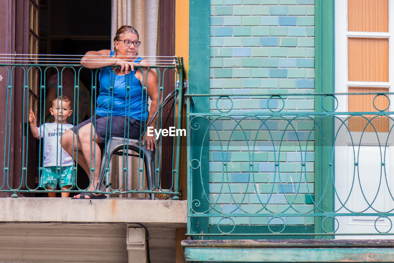 MAN SITTING ON RAILING AGAINST BLUE WALL