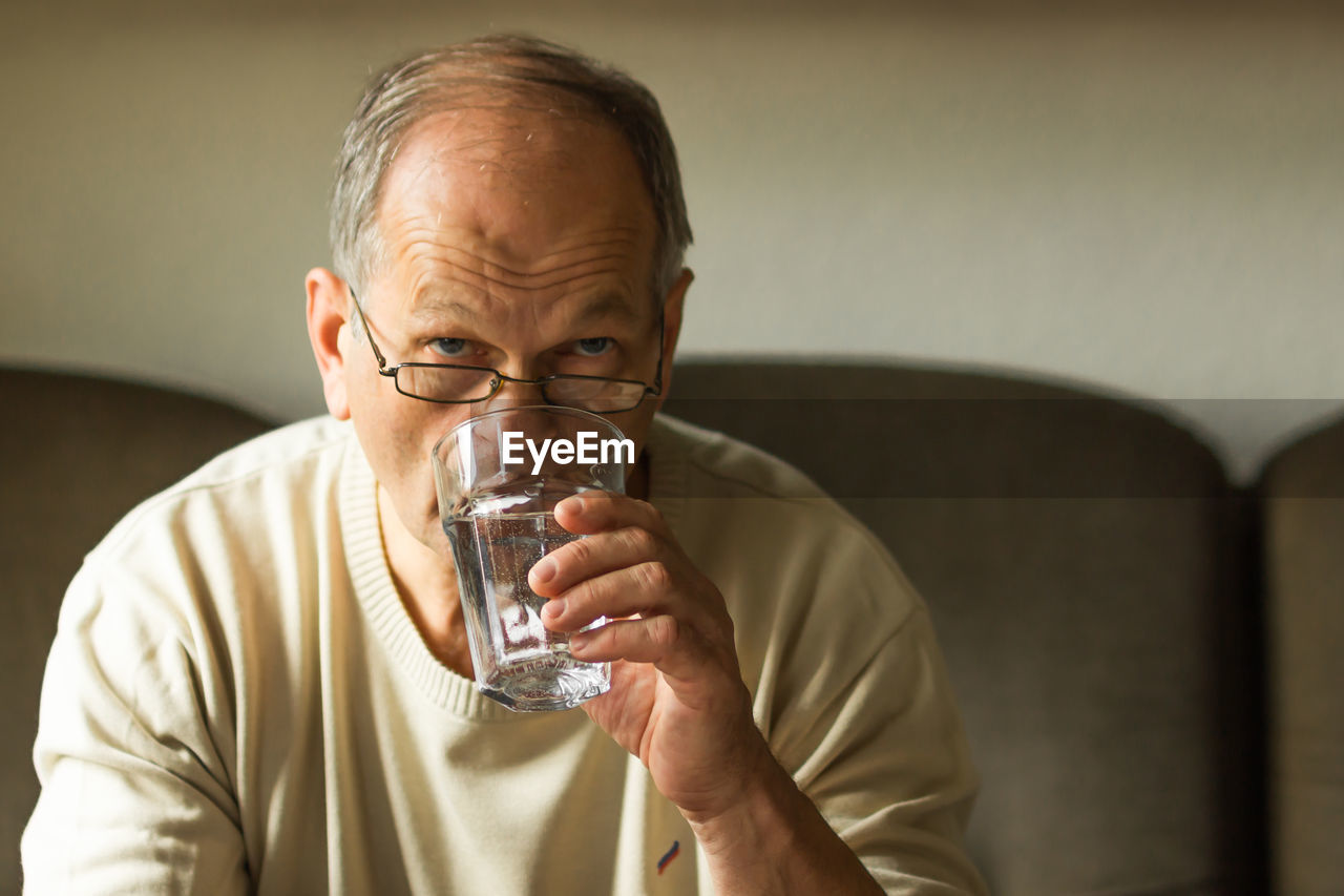 Caucasian senior man take capsule and drinking water from glass on sofa at home, feels like sick.