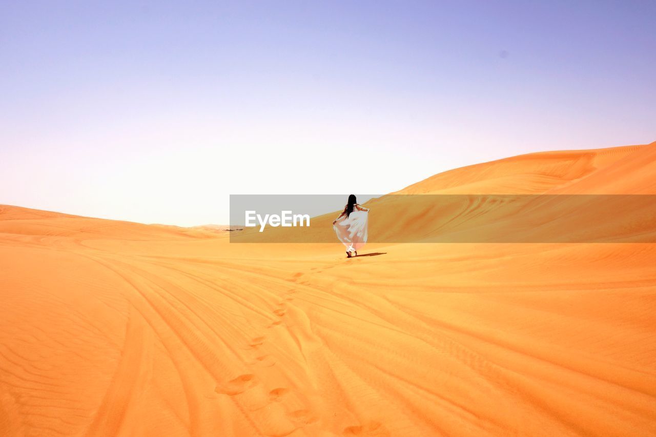 Rear view of woman walking in desert against clear sky