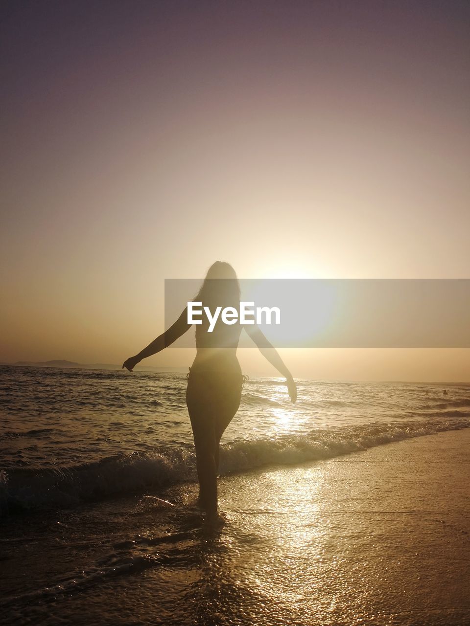 Silhouette woman standing at beach against sky during sunset