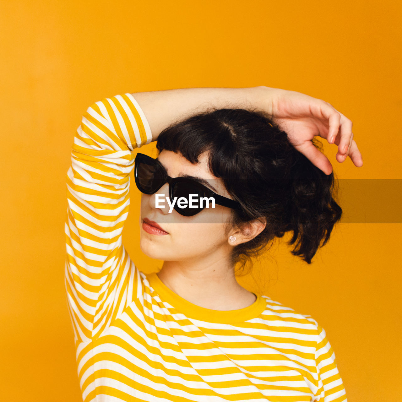 Young woman wearing sunglasses against yellow background