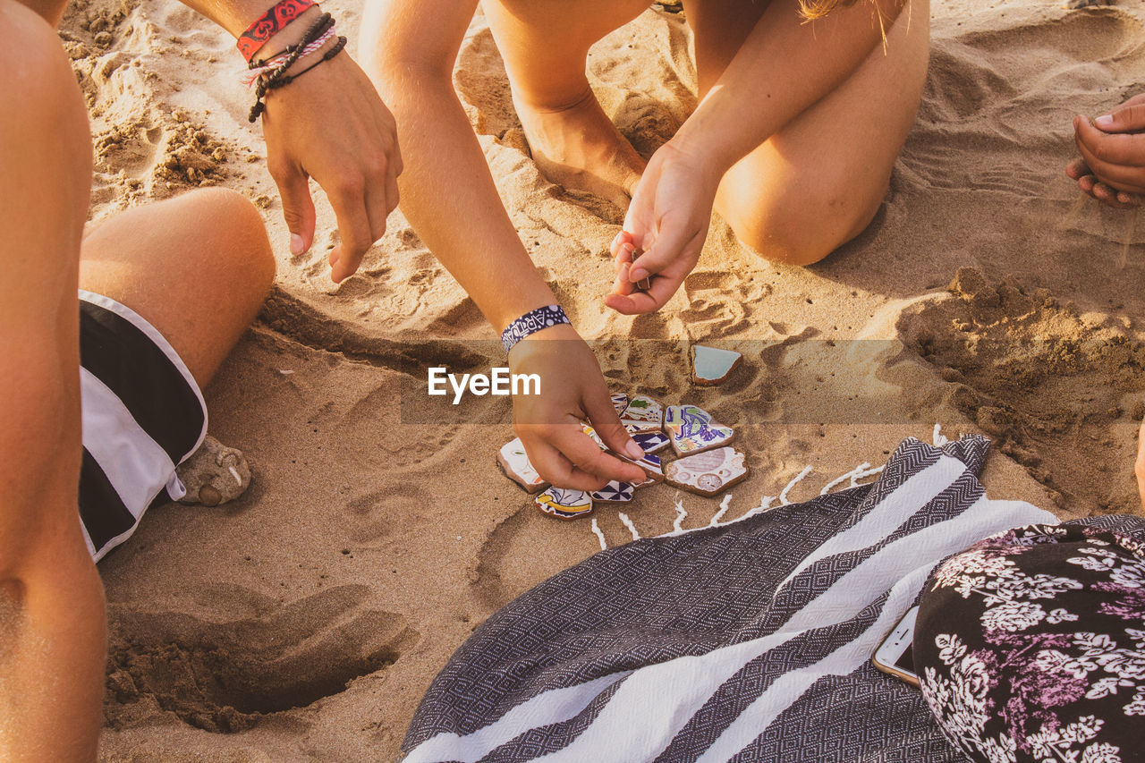 Woman with friend arranging tiles on sand at beach