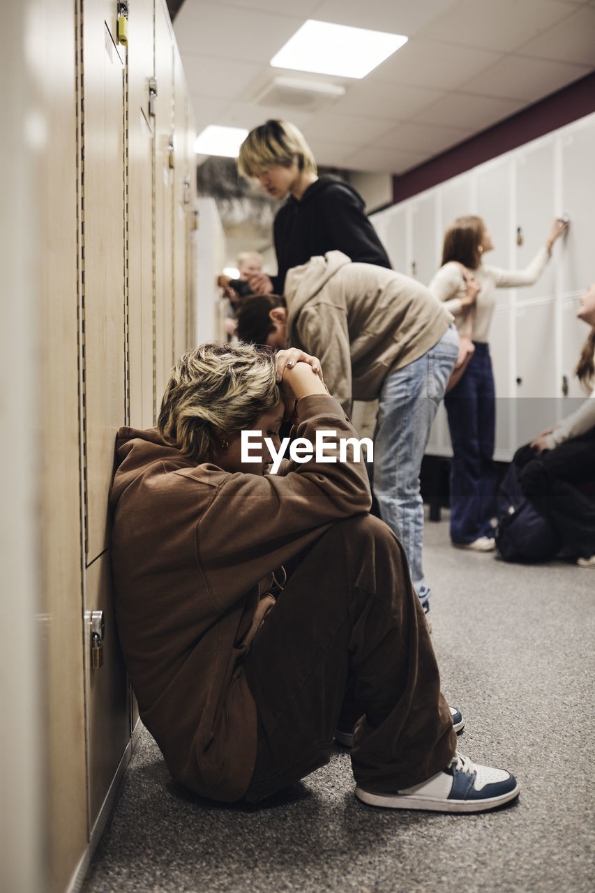 Side view of depressed teenage girl sitting by locker in school corridor