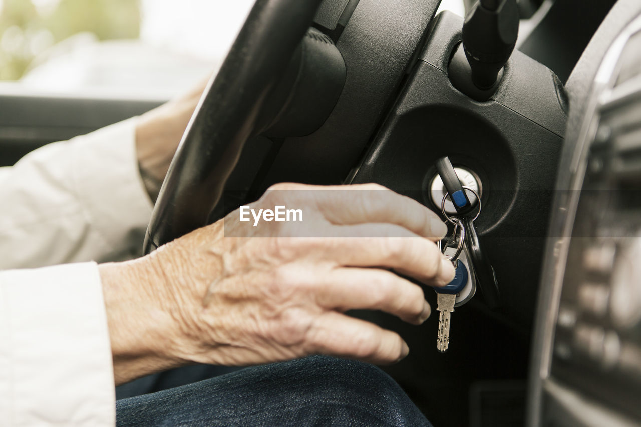Cropped image of senior woman putting car key in ignition lock