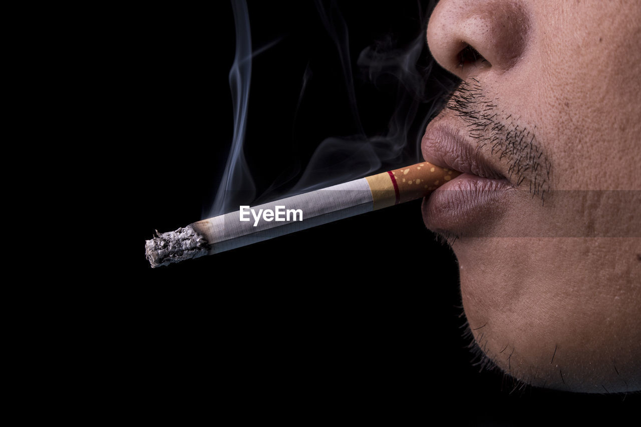 Cropped image of man smoking cigarette against black background