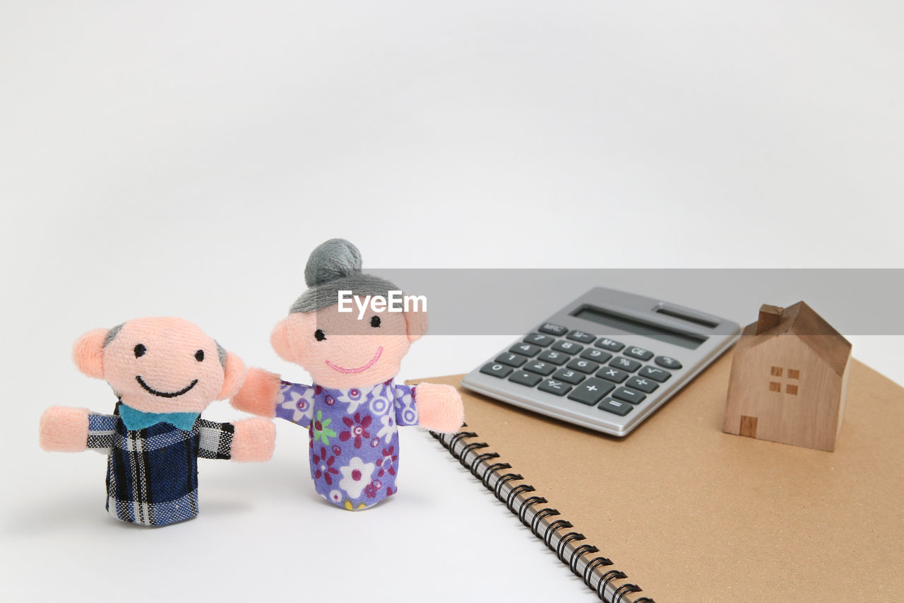 Close-up of figurines by spiral notebook and calculator against white background