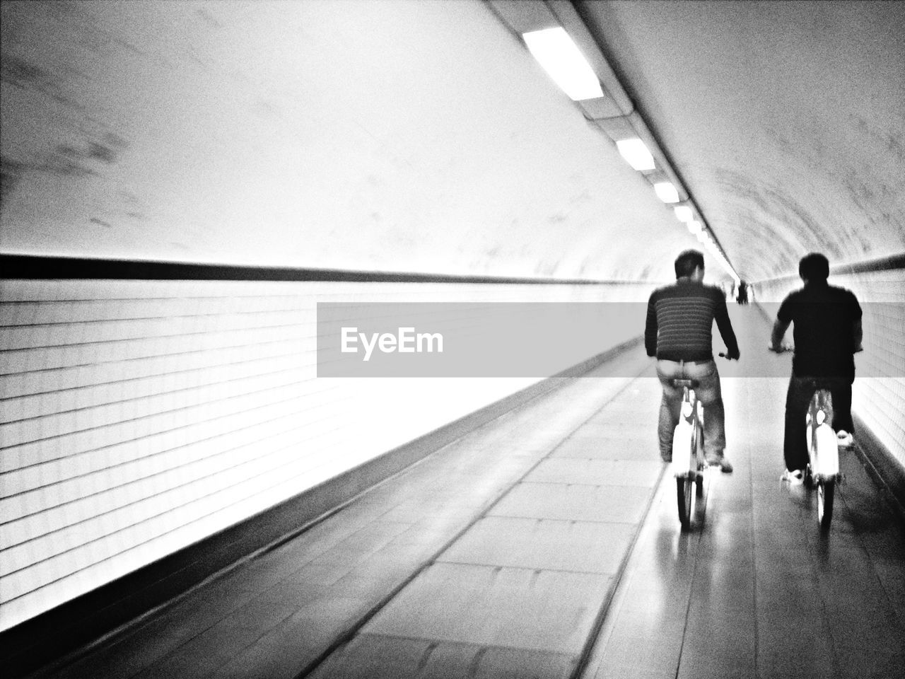 Rear view of men riding bicycle in tunnel
